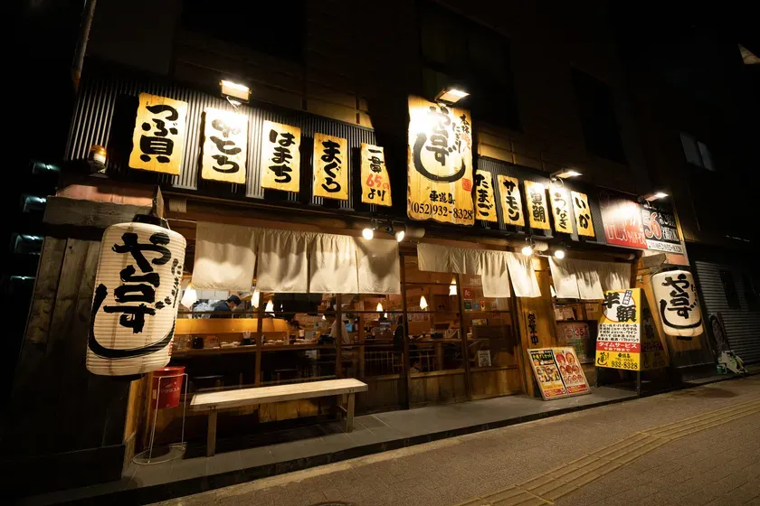夜の飲食店。提灯や看板に日本語で店名などが書かれている。店の外観を写した写真。