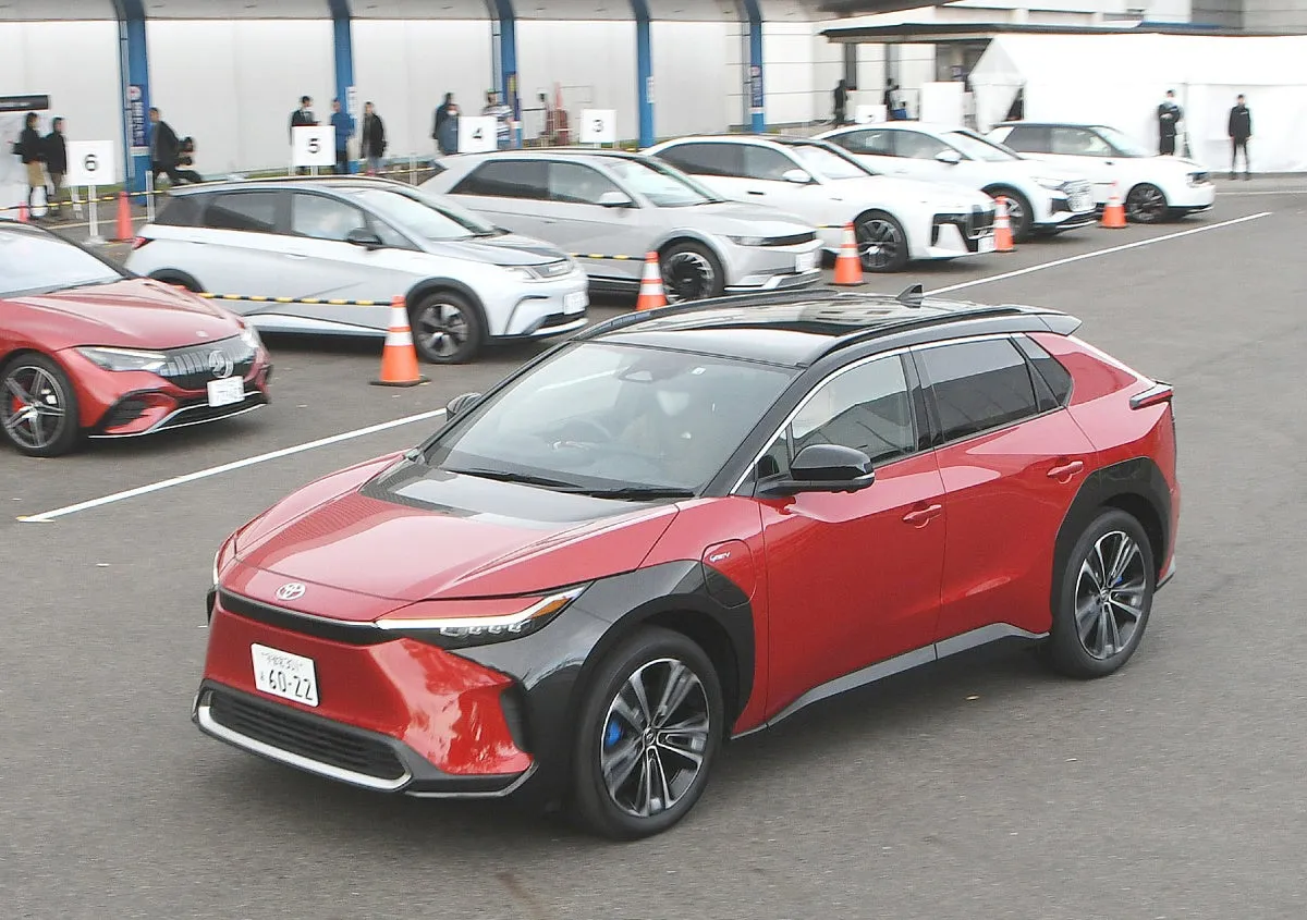 赤いトヨタ bZ4X EV 車が駐車場を走行しています。他の電気自動車が並んでいます。