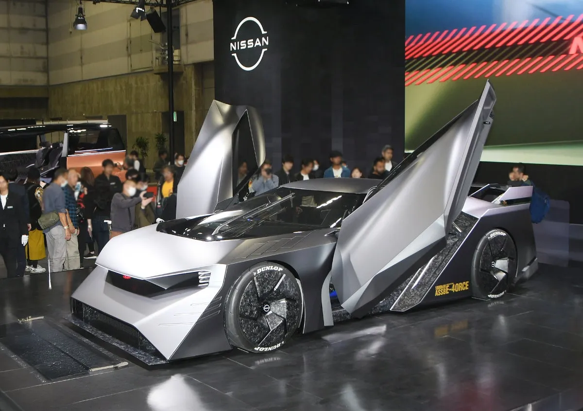 日産の未来的なコンセプトカーの展示。車体はグレーを基調とし、ガルウィングドアが特徴的。背景にはNISSANのロゴが掲げられ、多くの人々が車を取り囲んでいる。