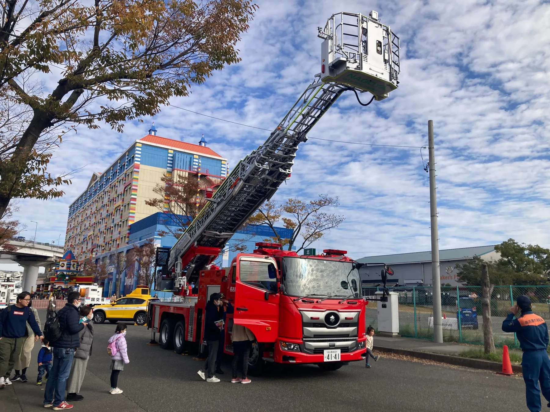 消防車と人々が写っている写真。消防車は赤い色をしており、長い梯子を伸ばしている。人々は消防車を見学しているようだ。