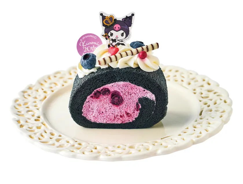 クロミの20周年を記念したロールケーキ。黒い生地にピンク色のクリームが詰められ、ブルーベリーやクロミの飾りでデコレーションされている。白いレース模様の皿に盛り付けられている。