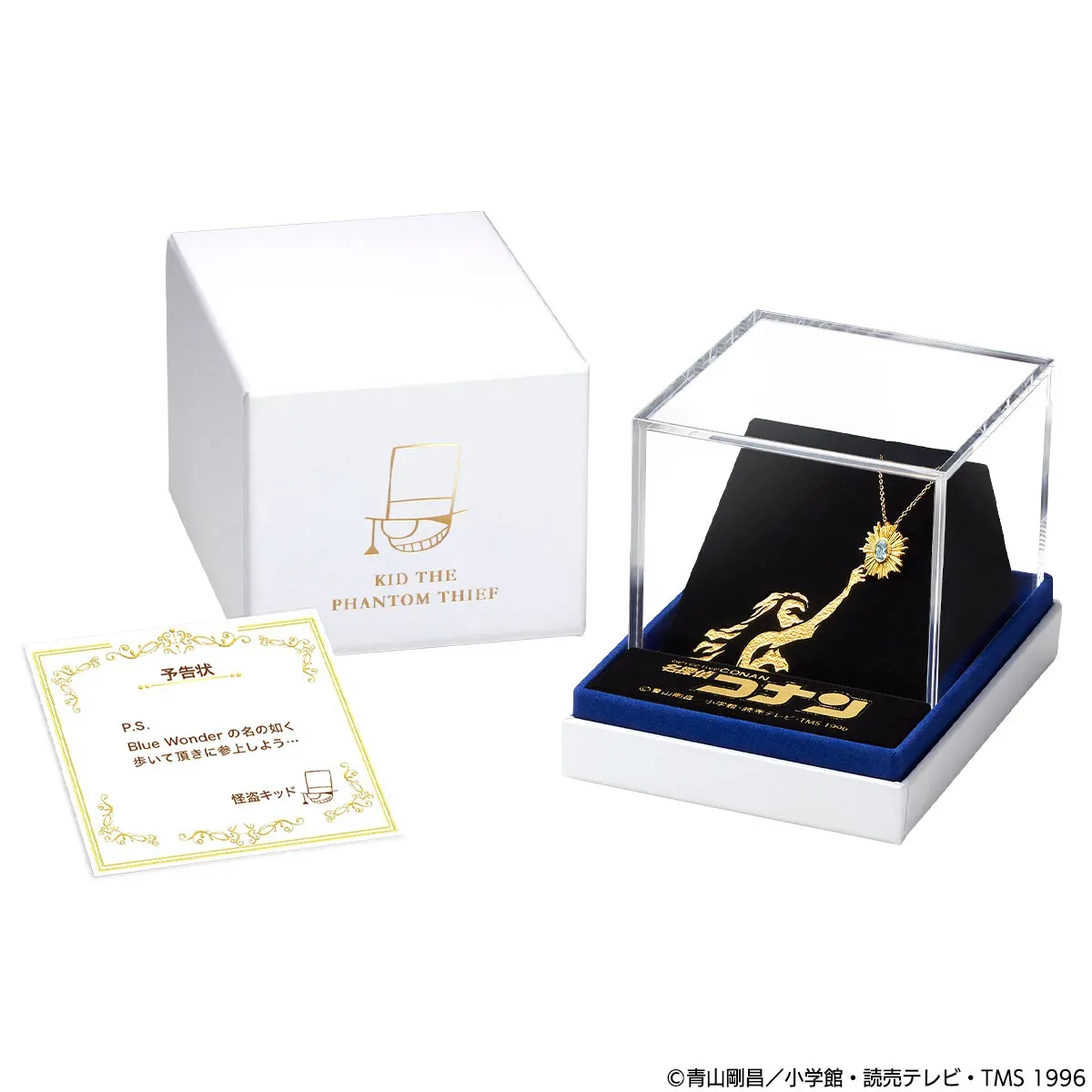 白い箱と透明なケースに入った、怪盗キッドのネックレスのセット。ネックレスは金色で、青い石が輝いている。箱には怪盗キッドのロゴが、ケースの台座には怪盗キッドのシルエットが描かれている。手前には予告状が置かれている。