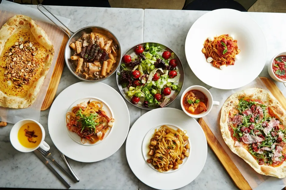 テーブルの上に、ピザ、パスタ、サラダ、スープなど様々な料理が並べられた写真。