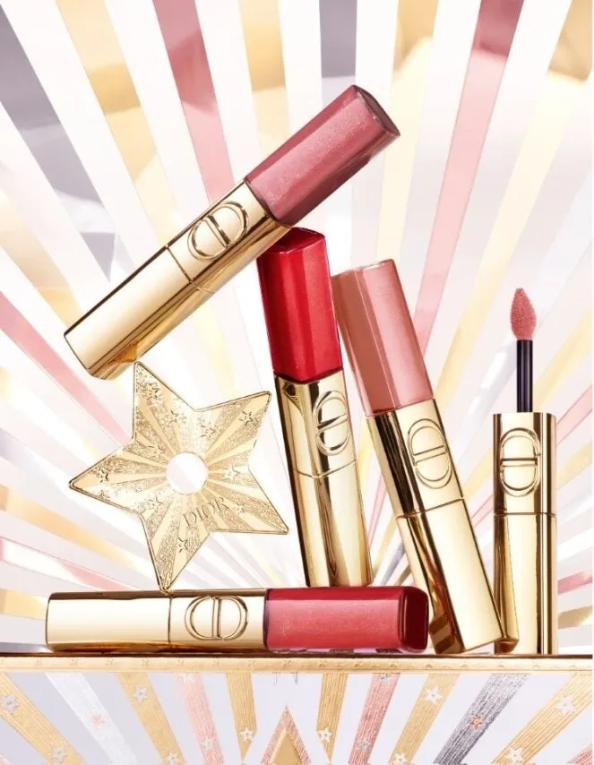 Diorの化粧品が写った画像。リップグロスとリップスティックが、金色の星の装飾と共に配置されています。背景は光沢のあるストライプ模様で、華やかな印象を与えています。