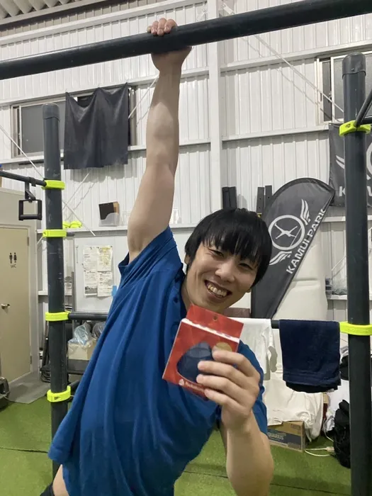懸垂をする男性が、何か商品を持って微笑んでいる様子