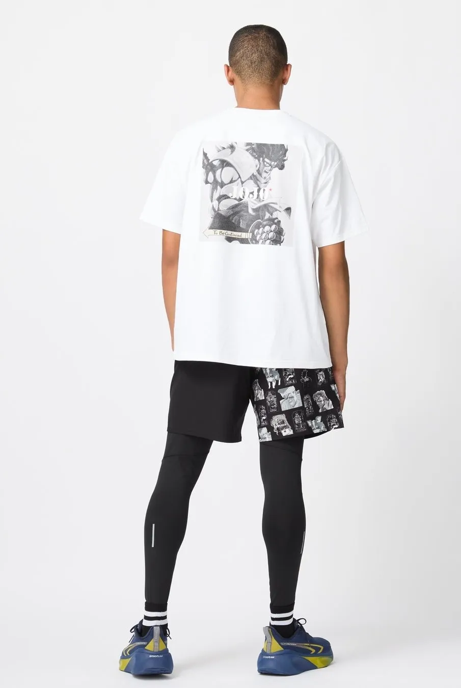 ジョジョの奇妙な冒険のイラストがプリントされたTシャツと黒のショートパンツ、レギンスを着用した後ろ姿の男性
