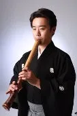 尺八を吹いている男性のポートレート写真です。彼は伝統的な日本の衣装を着ています。