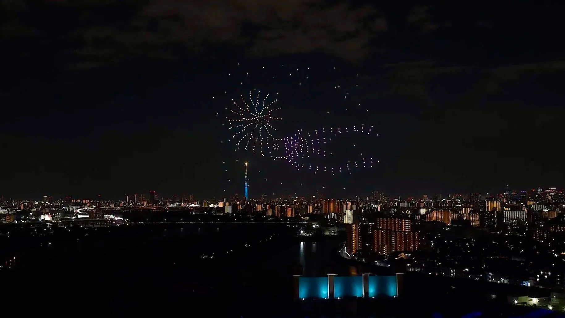 夜空に花火のような光の演出が行われている様子が写っています。東京スカイツリーも見えることから、東京の夜景と思われます。