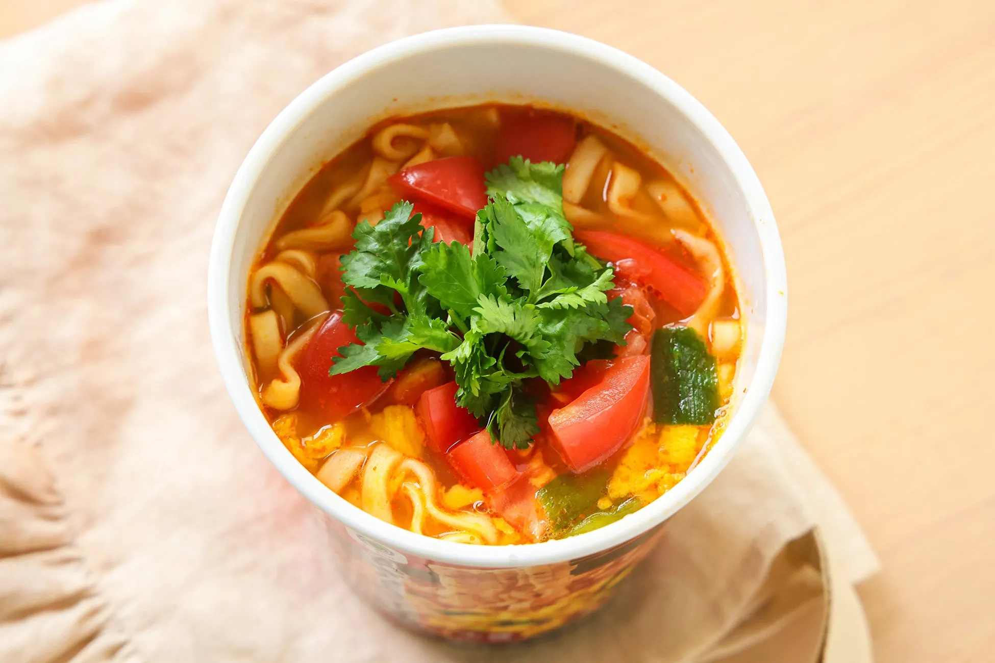 トマトとパクチーがトッピングされたラーメンのクローズアップ写真。