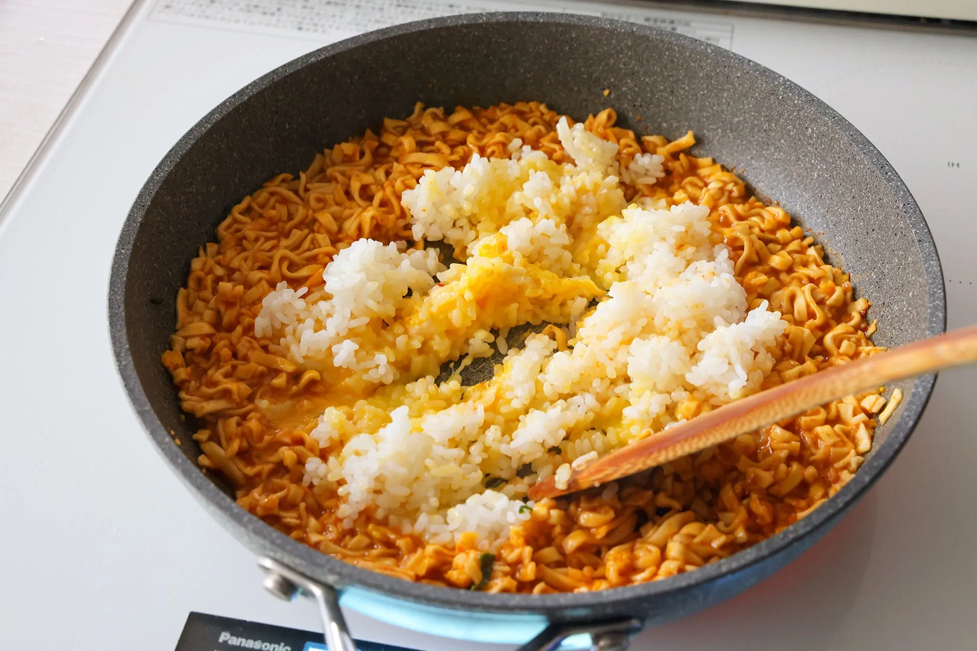 フライパンで調理された料理の写真。インスタントラーメンとご飯を混ぜて調理している様子。