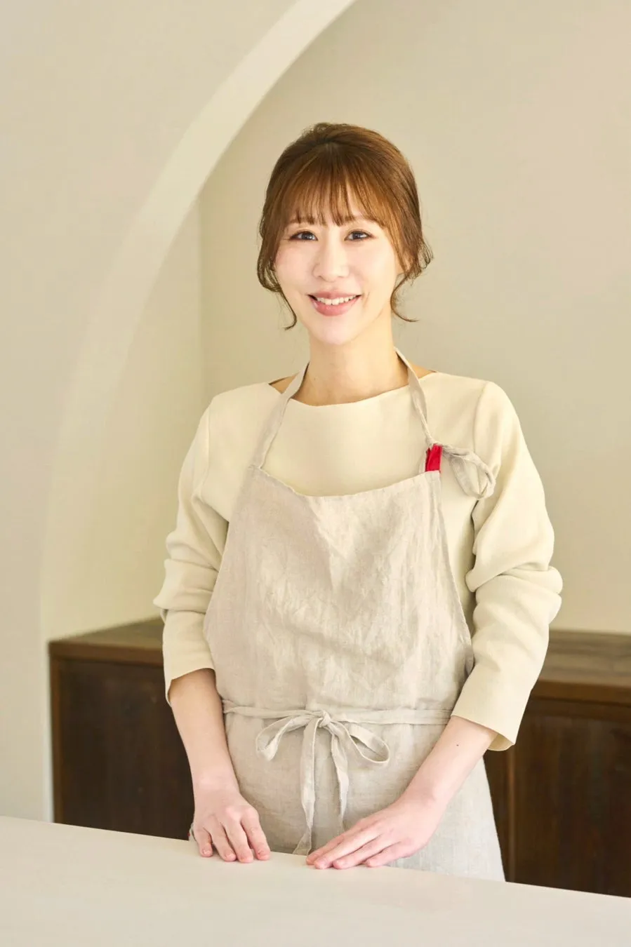 エプロンを着た女性が笑顔で立っている様子。