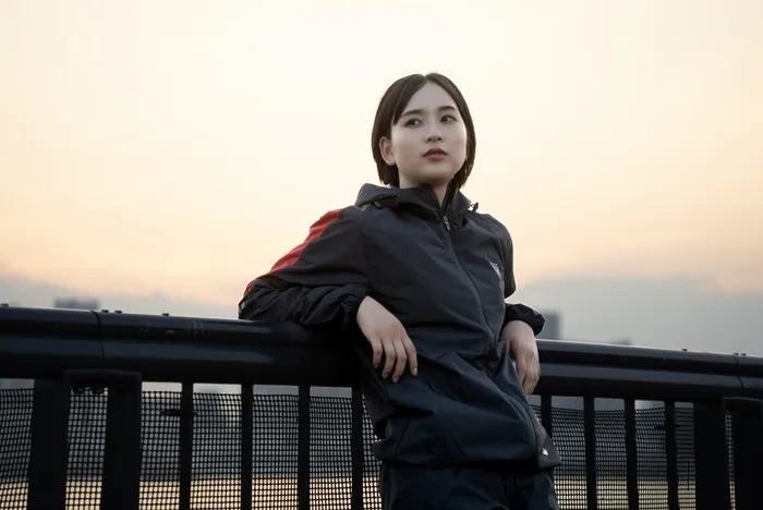 夕焼けを背景に、手すりに寄りかかって遠くを見つめる女性の写真。