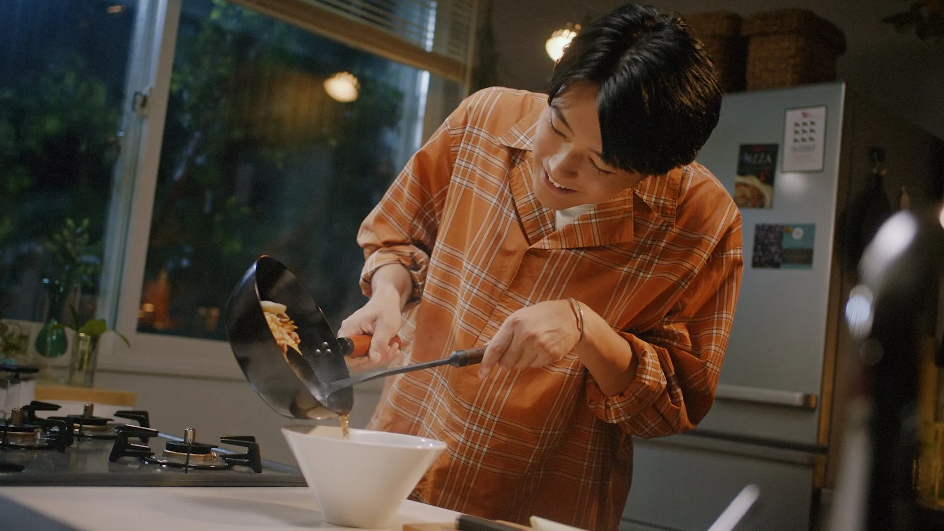 男性がキッチンで料理をしている様子。フライパンから料理をボウルに盛り付けている。