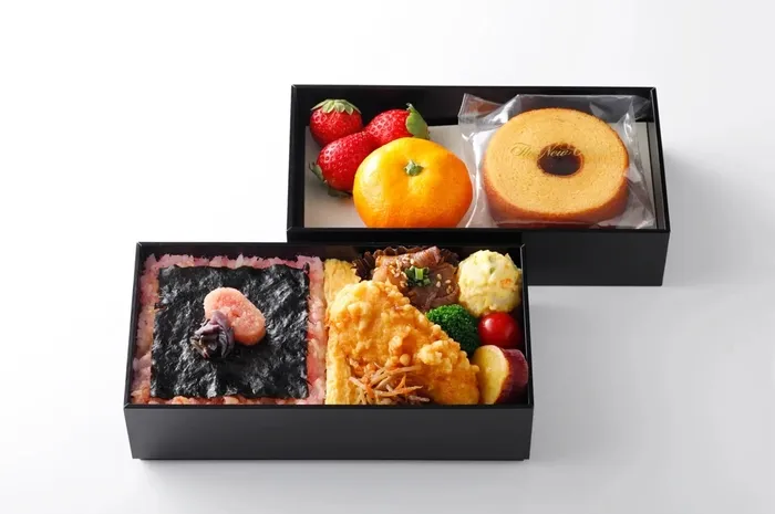 弁当のイメージです。上段には、いちご、みかん、バームクーヘン、下段には、ご飯、明太子、海苔、卵焼き、揚げ物、肉、野菜などが入っています。