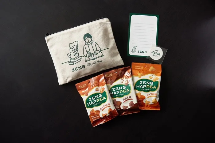 黒いテーブルの上に、ZENB HAPPEAのスナック菓子3種類、ZENBのロゴが入ったポーチ、メモ帳、ステッカーが配置された写真。