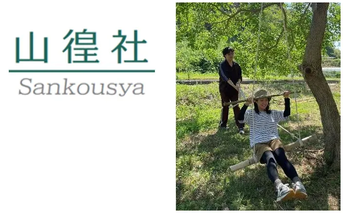 ブランコに乗って遊んでいる女性と、それを見守る男性が写っている写真です。