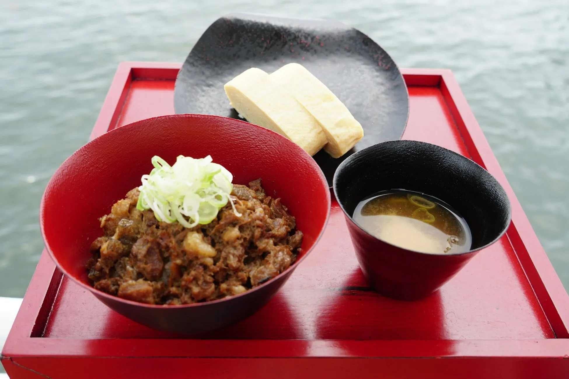 赤いお盆に、牛丼のようなもの、卵焼き、味噌汁が乗った和食のセット。