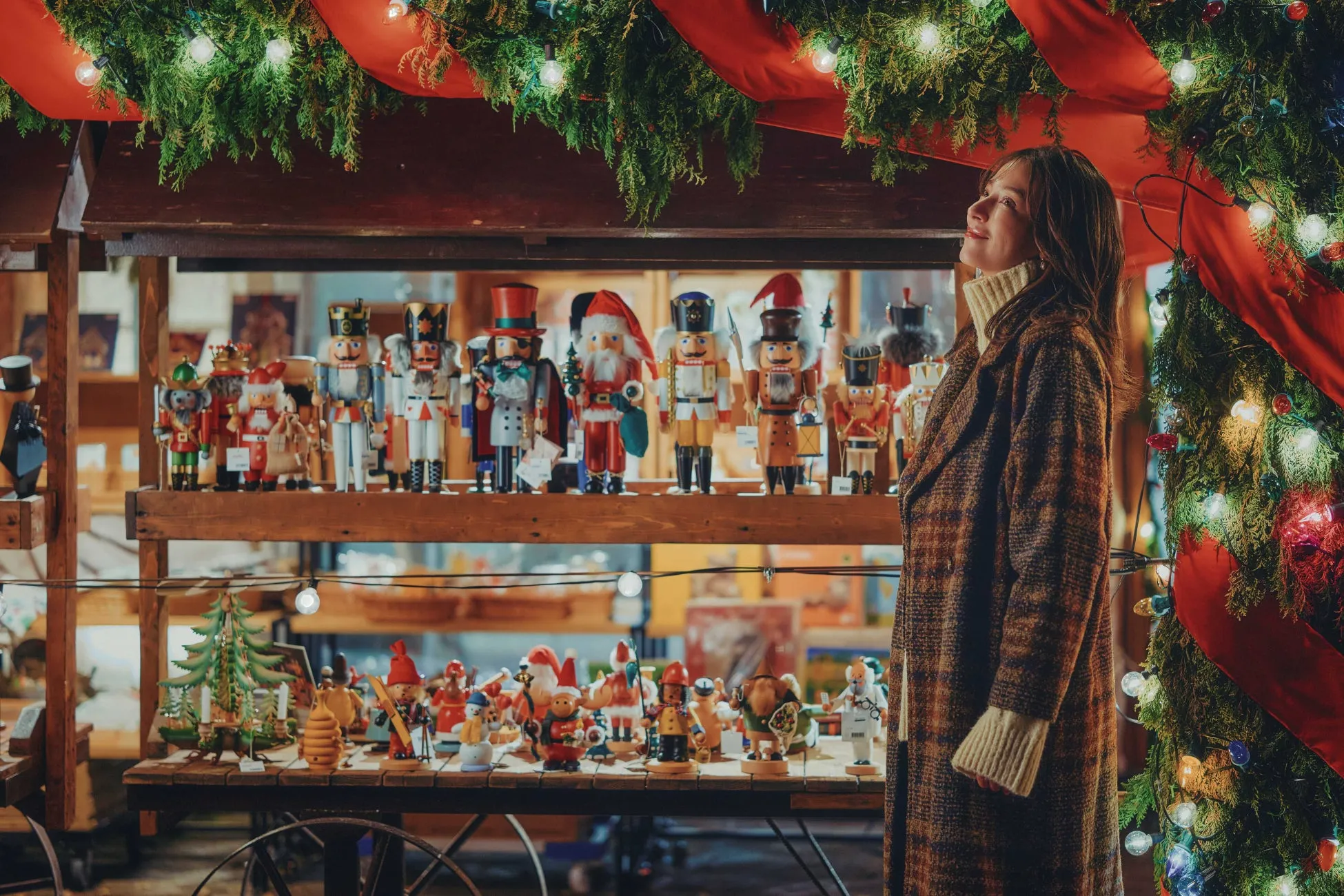 女性がクリスマスの飾り棚を見上げている様子を描いた写真。棚にはくるみ割り人形やクリスマスの飾り、電飾が飾られており、クリスマスの雰囲気を醸し出している。