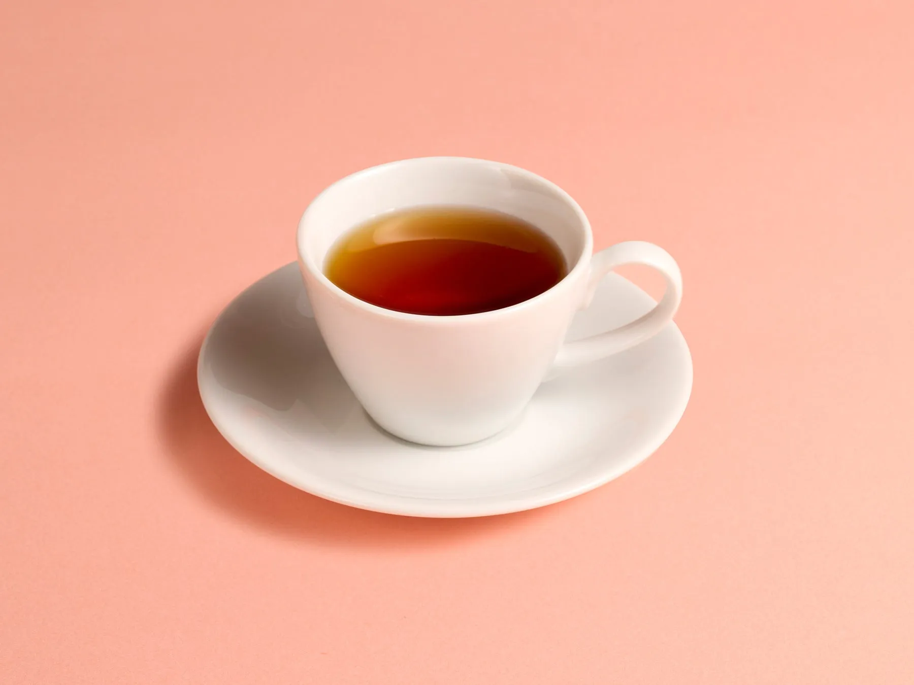 ピンク色の背景に、紅茶が入った白いカップとソーサーが置かれた写真。
