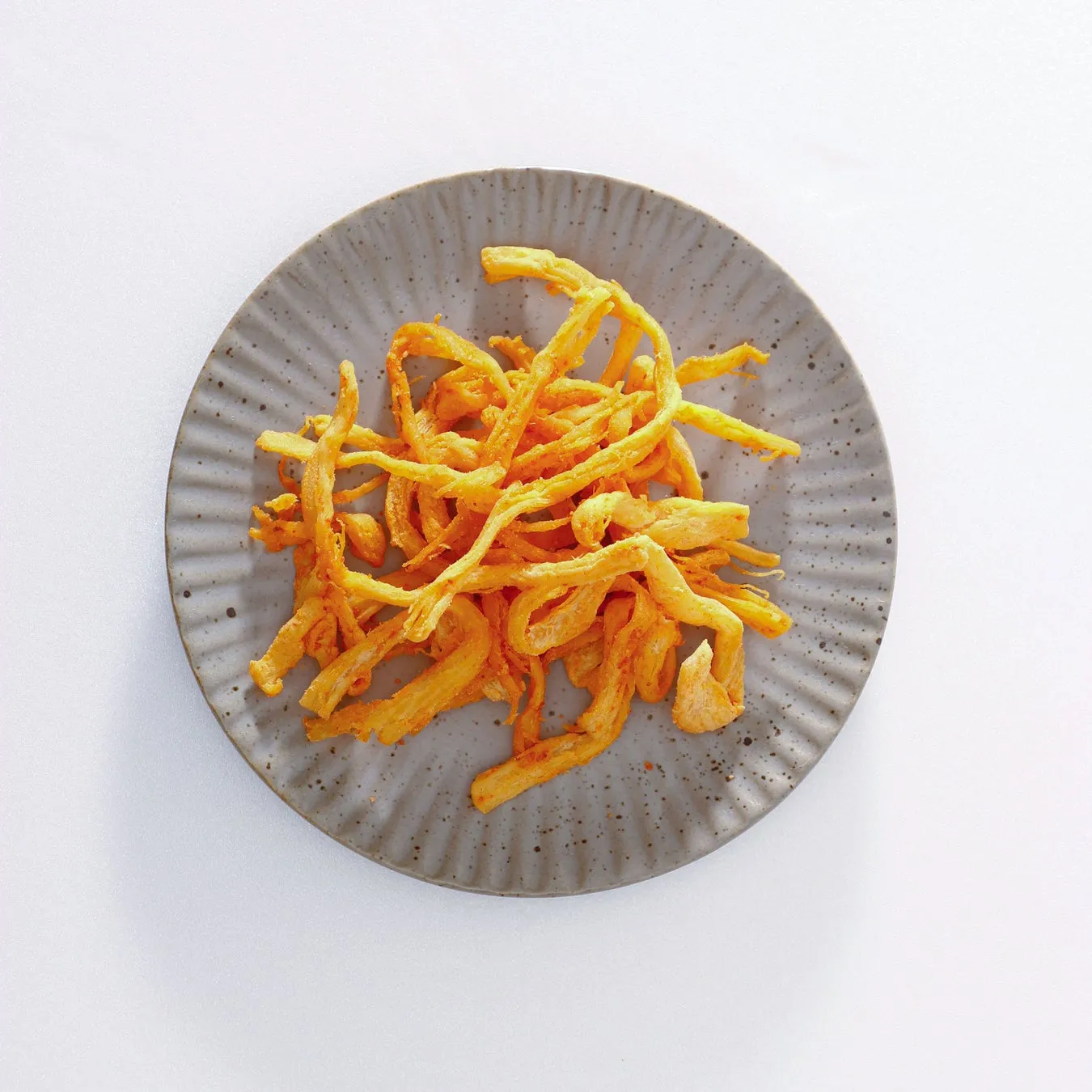 皿に盛られた揚げ物。黄色とオレンジ色の揚げ物がグレーの皿の上に置かれています。背景は白。