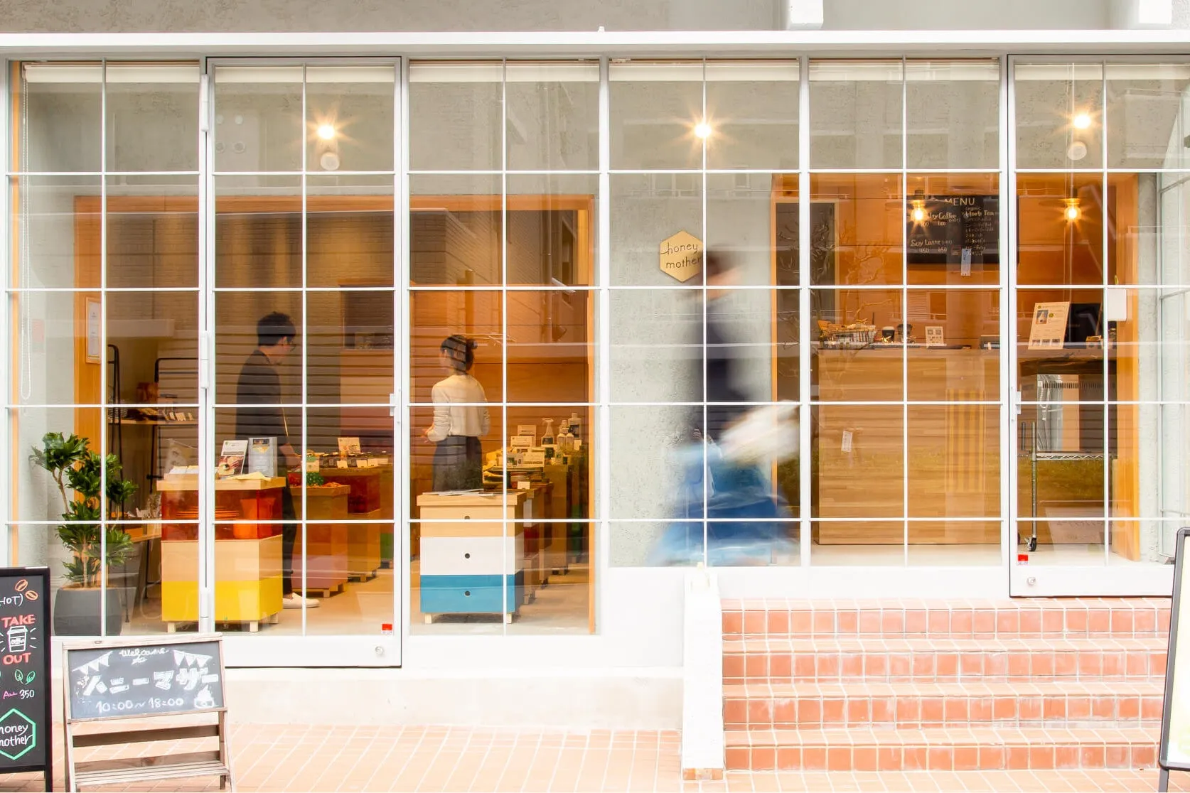 ガラス張りの店の外観。店員や商品が見え、看板には営業時間の記載がある。