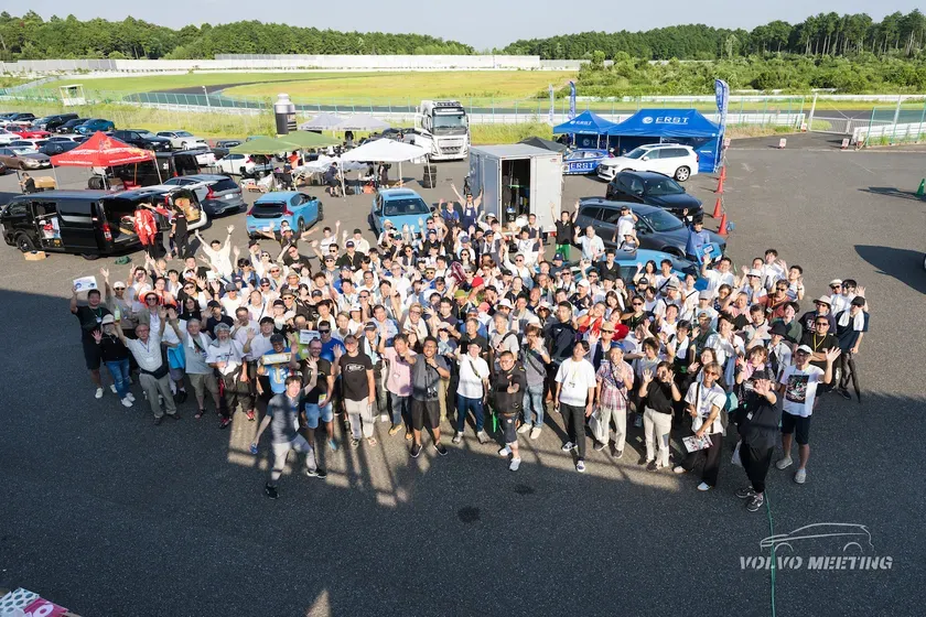 サーキットに集まったヴォルヴォオーナーたちの集合写真。多くの人が手を振っている。