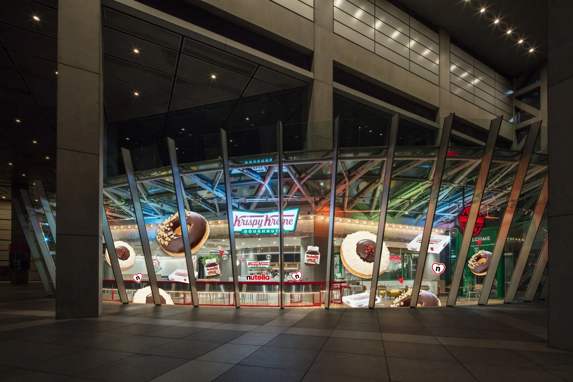 Krispy Kremeのドーナツショップの夜景。店構えには大きなドーナツの装飾や、Nutellaとのコラボレーションが示されている。