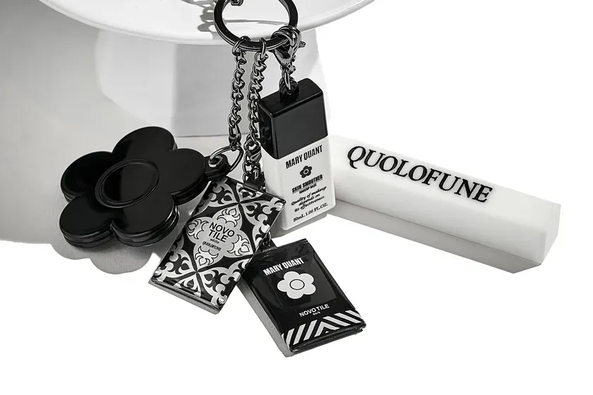 白黒を基調とした、キーホルダーや化粧品のようなアイテムが写った写真。 MARY QUANTのロゴや、花のモチーフが特徴的。