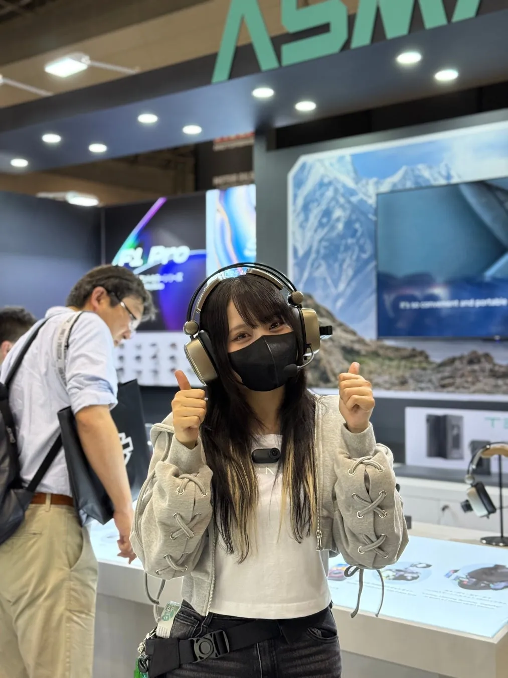 展示会でヘッドホンを着けた女性が親指を立てている様子。