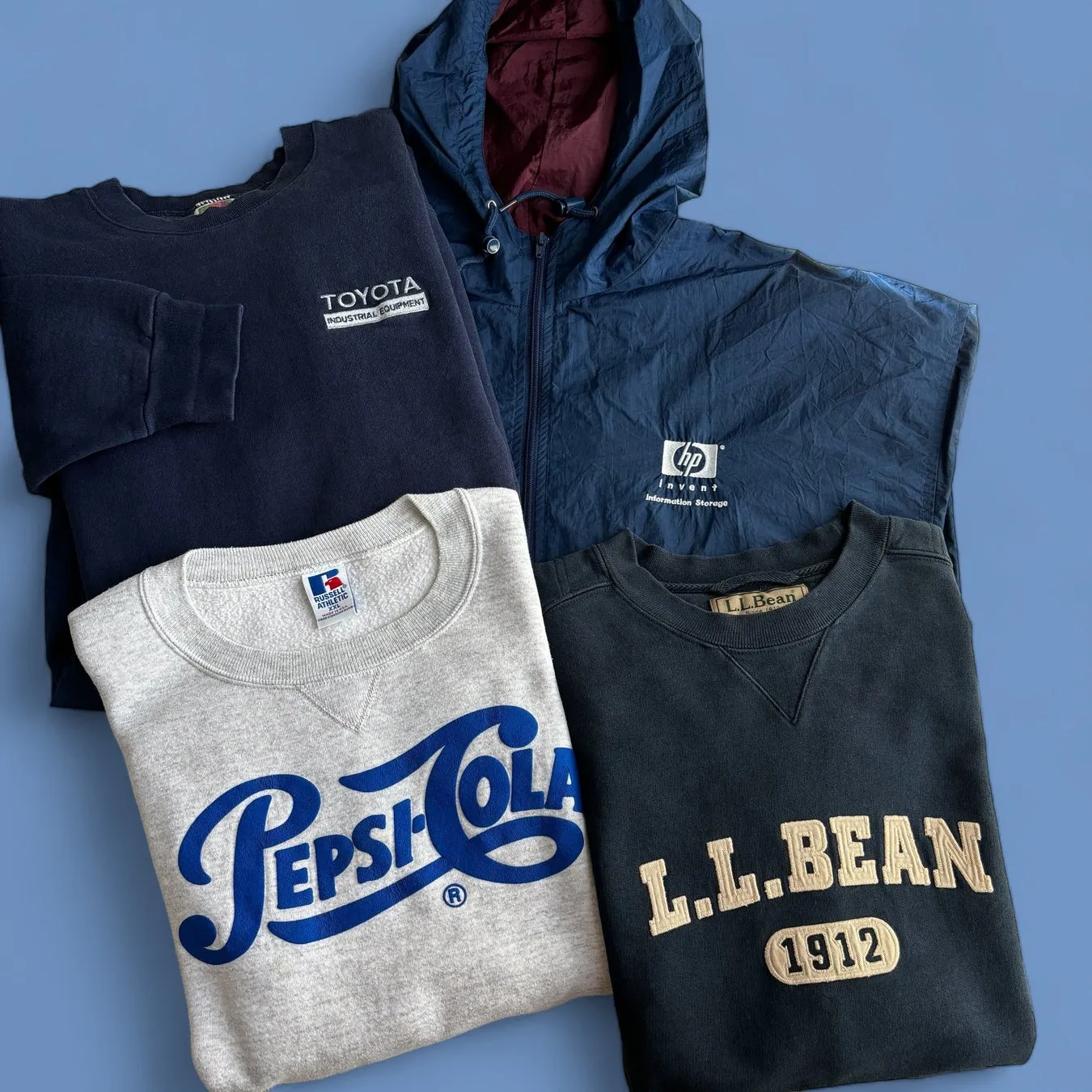 さまざまなブランドの服が重ねて配置された画像。トヨタ、HP、ペプシコーラ、L.L.Beanなどのロゴが入ったスウェットシャツとジャケットが写っています。