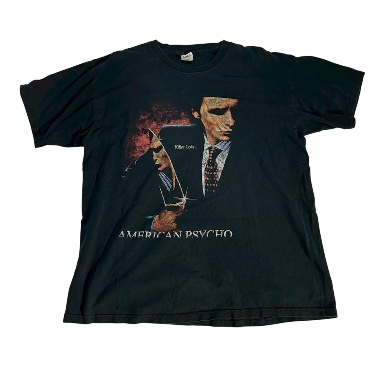 黒色のTシャツ。前面には、映画「アメリカン・サイコ」のポスターがプリントされています。主人公のパトリック・ベイトマンが描かれ、「Killer looks.」と「AMERICAN PSYCHO」の文字が記されています。