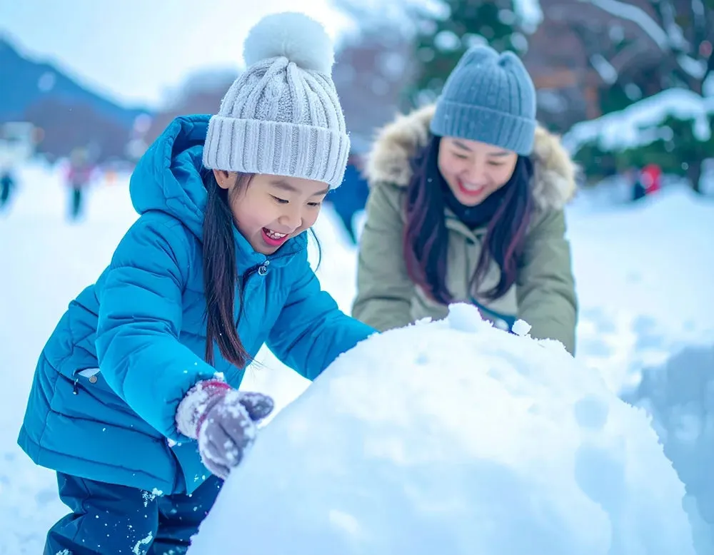 雪の中で雪玉を作る親子。