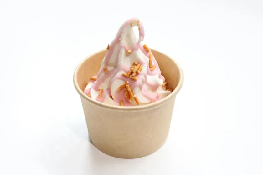 紙カップに入ったソフトクリーム。ピンクのソースとトッピングがかけられている。