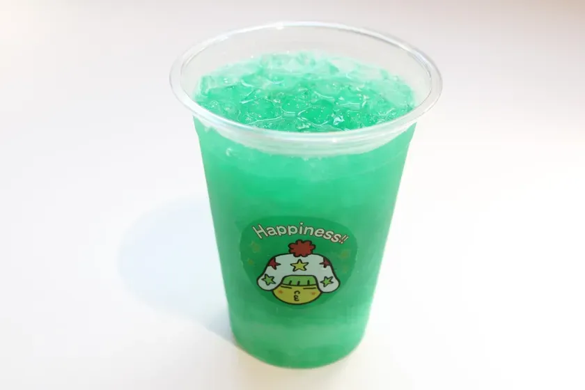 透明なプラスチックカップに入った緑色の飲み物。氷が入っていて、ラベルには「Happiness!!」と書かれたキャラクターが描かれています。