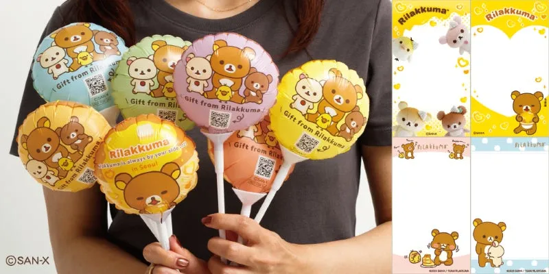 リラックマの風船とメモ帳を持った女性の画像です。風船には「Gift from Rilakkuma」の文字とQRコード、リラックマのイラストが描かれています。メモ帳にもリラックマのイラストが描かれています。