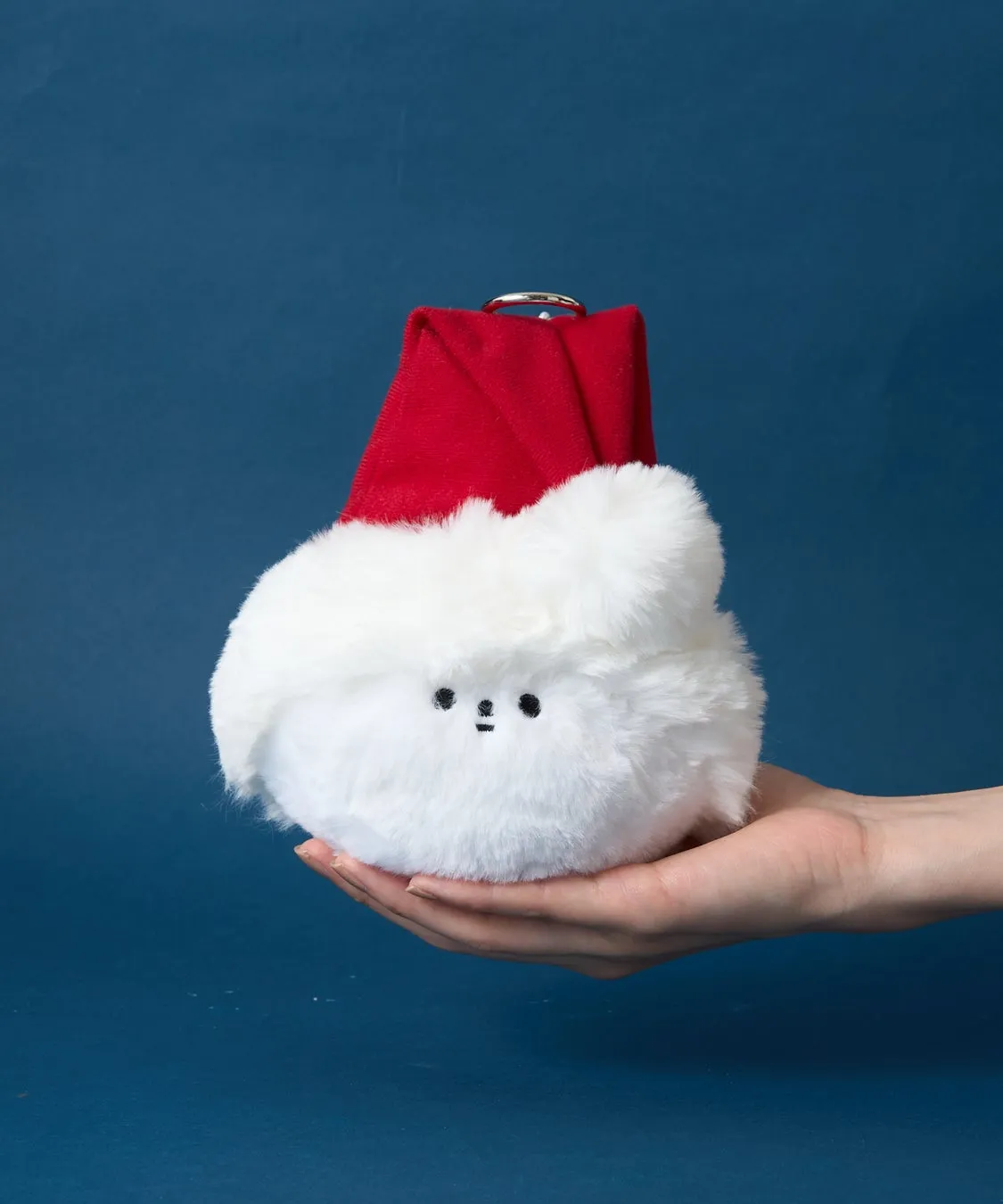 サンタ帽をかぶった白いふわふわのキャラクターが、手のひらに乗せられている写真です。背景は青色です。