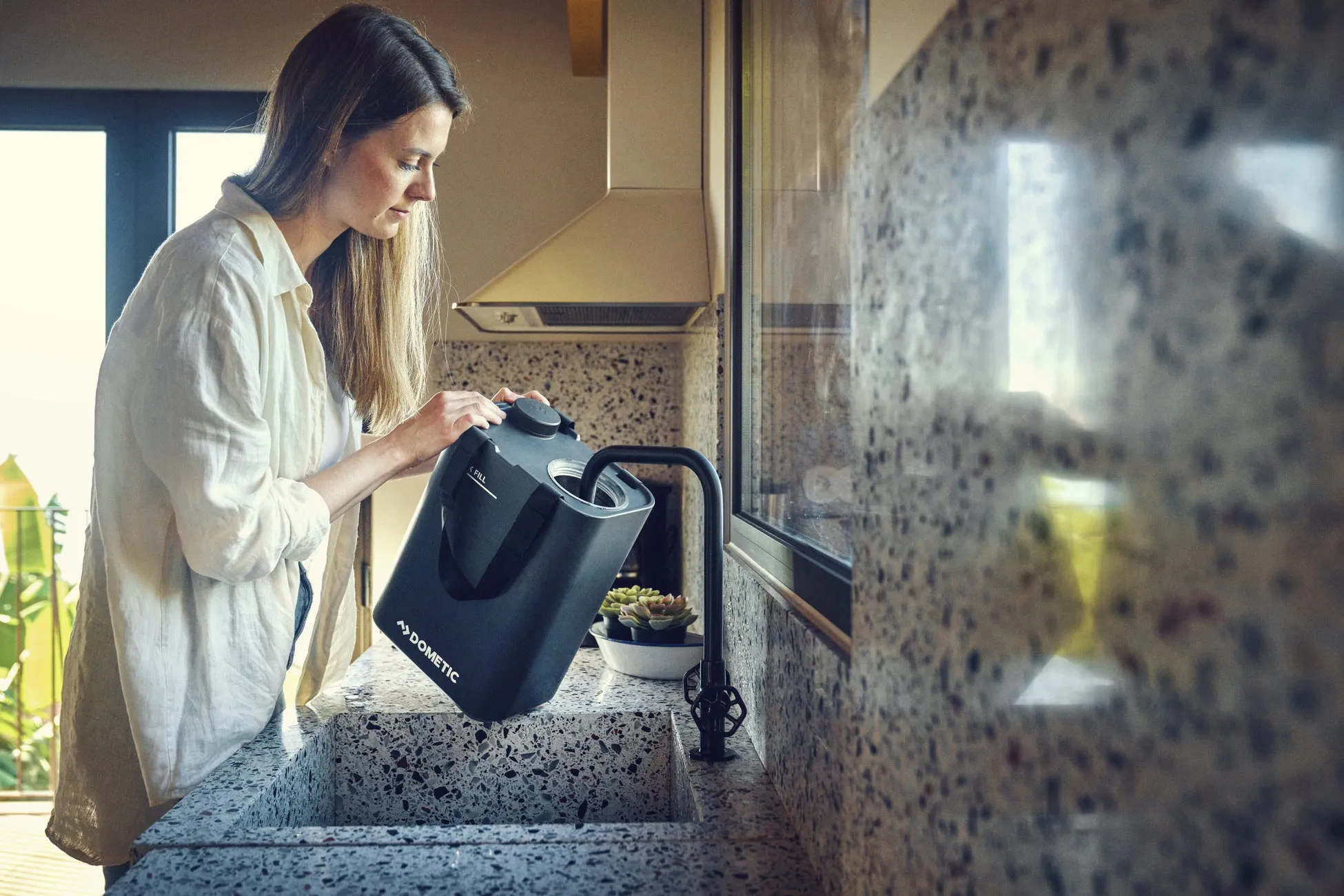 女性がキッチンで水筒に水を注いでいる様子。