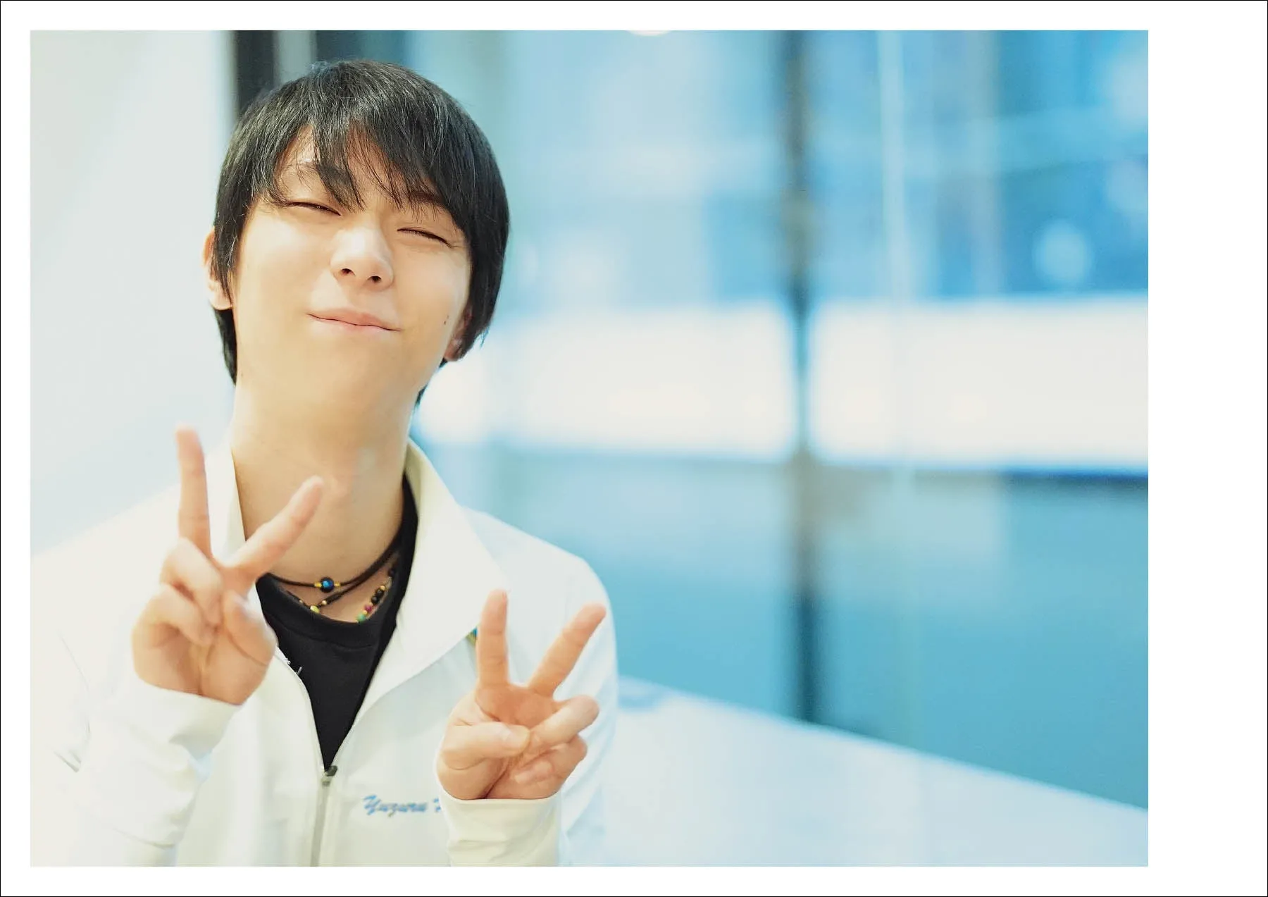 ピースサインをする羽生結弦選手の写真。白いジャケットを着ており、穏やかな表情をしている。