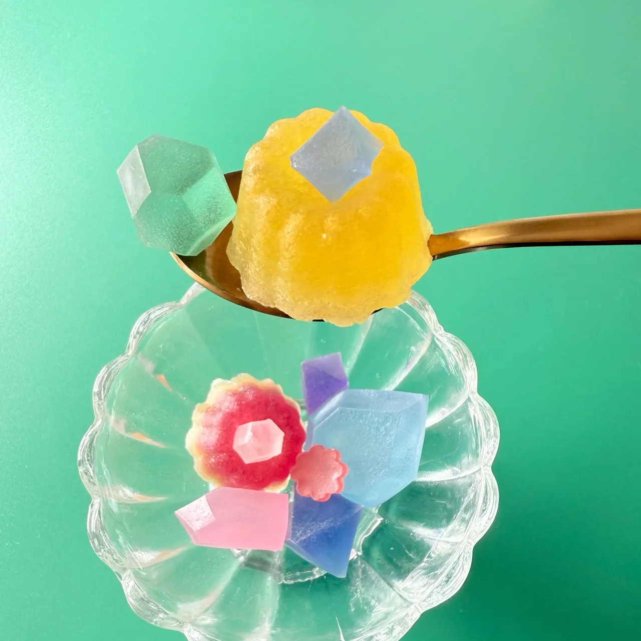カラフルな和菓子が、スプーンとガラスの器に盛られた写真。鮮やかな色合いと、涼しげな雰囲気が特徴的。