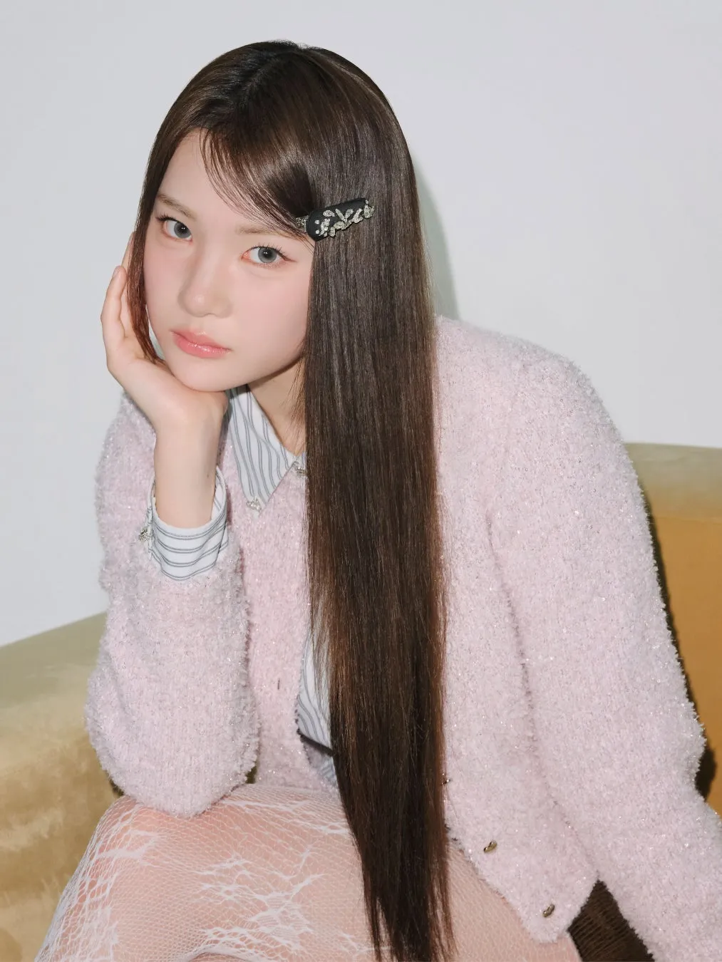 女性がポーズを取っているポートレート写真。彼女は長い茶色の髪をしており、髪留めが付いている。彼女はピンクのジャケットを着ており、白いレースのストッキングを履いている。