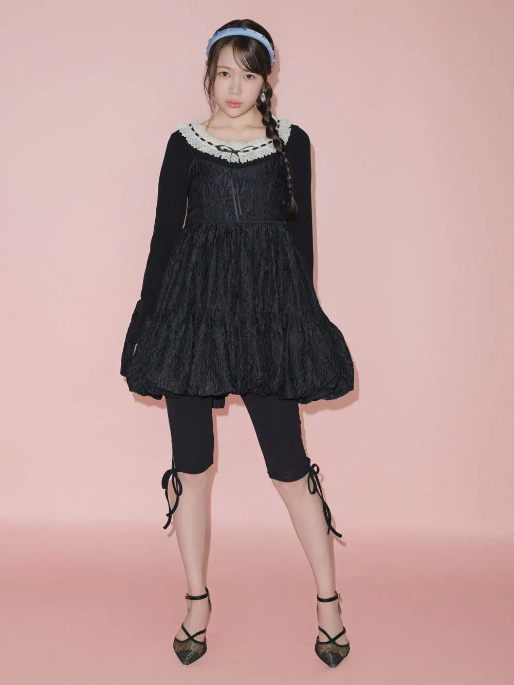 ピンク色の背景に、黒いドレスを着た女性が立っている写真。