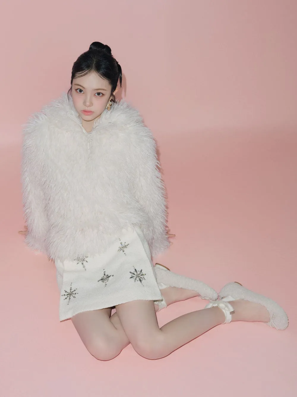 ピンクの背景に座っている若い女性。白い毛皮のコートと雪の結晶模様のスカートを着ています。