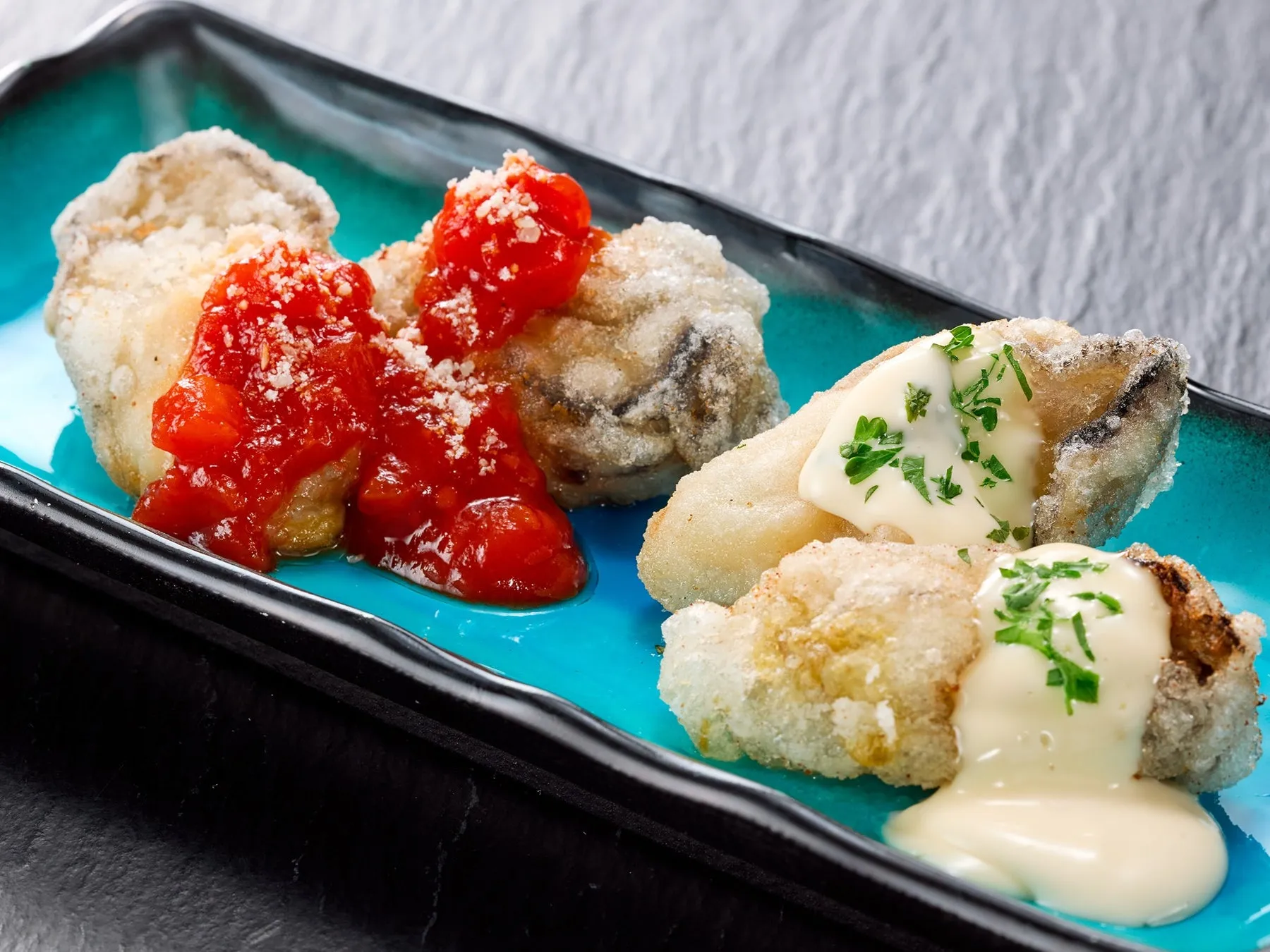 揚げ物料理が青い皿に盛り付けられている写真です。揚げ物にはトマトソースと白いソースがかかっています。