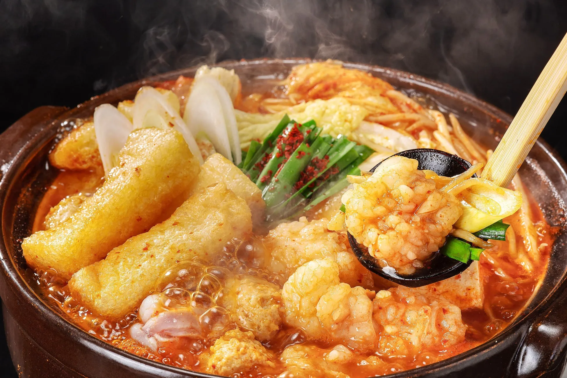 熱々の鍋料理の写真。具材には、揚げ豆腐、ネギ、ニラ、キムチ、モツなどが入っており、湯気が立っている様子から、出来立てであることがわかる。