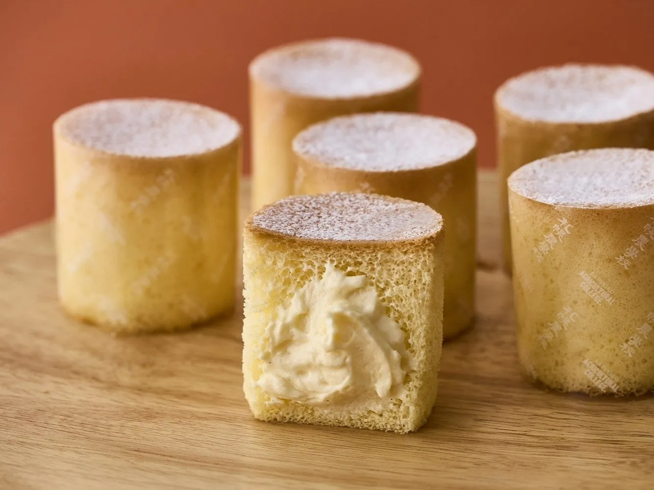 丸い形のケーキが木製のプレートの上に並べられています。ケーキは、クリームが詰められたものと、粉砂糖がまぶされたものがあります。