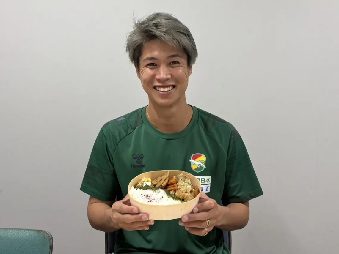 弁当を持った男性が笑顔でカメラに向かっている様子。