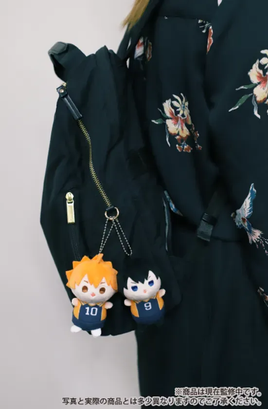 黒いリュックに、オレンジと黒のキャラクターのぬいぐるみが2つぶら下がっている写真。服には花柄と鳥の模様が描かれている。