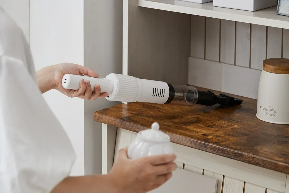 女性が掃除機を使って棚を掃除している様子。棚にはコーヒーカップのイラストが入った容器が置かれている。