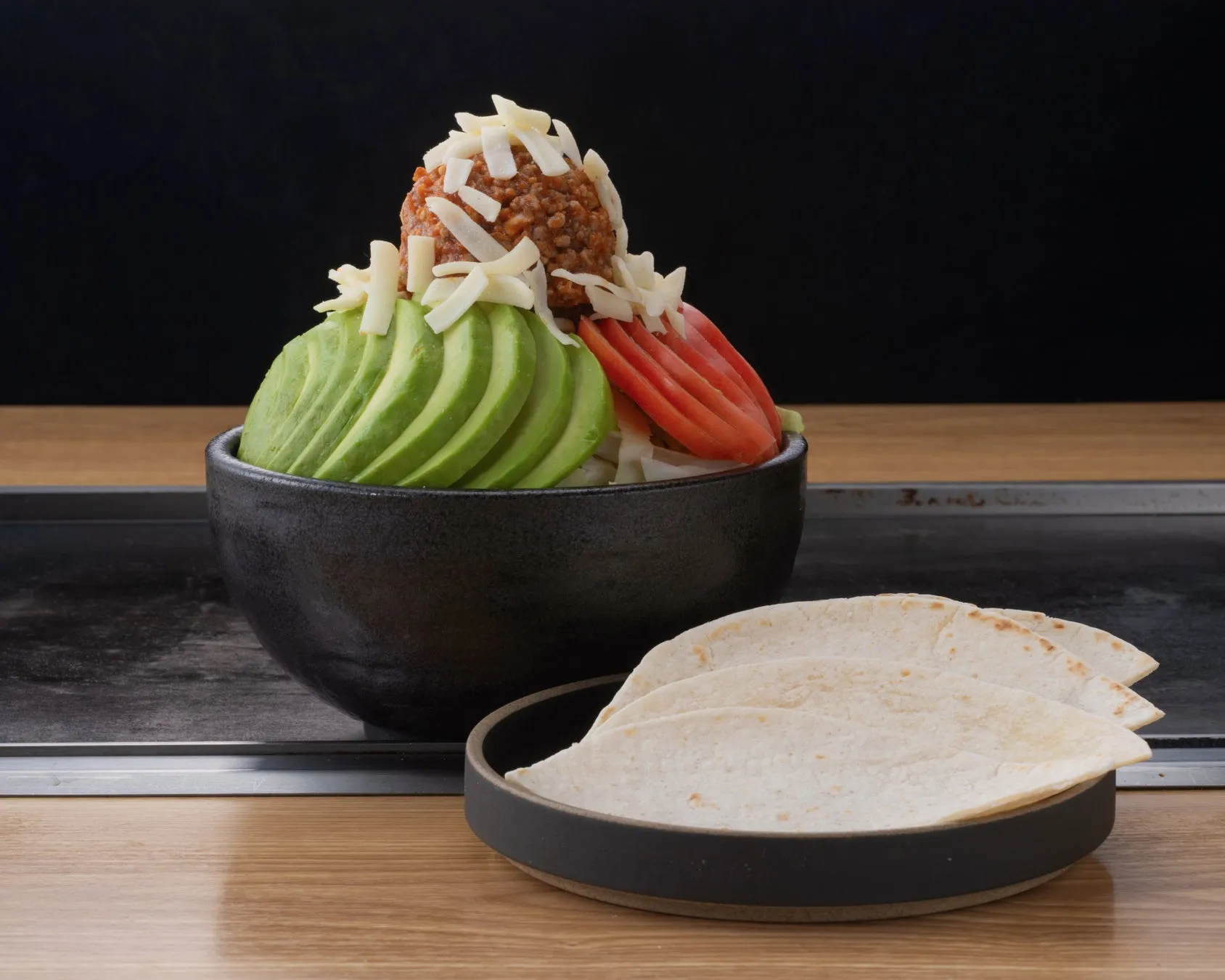 アボカド、トマト、ひき肉、チーズが乗った料理とトルティーヤの画像。