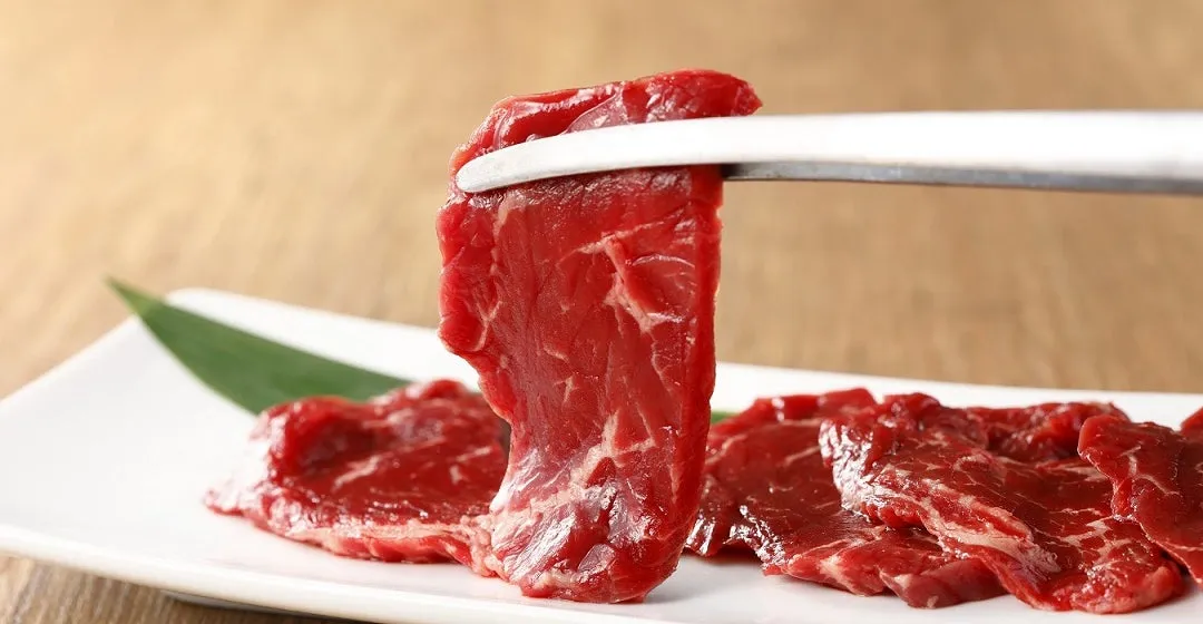 お皿に盛られた焼肉の写真です。トングで持ち上げられた一枚と、他数枚のお肉が写っています。